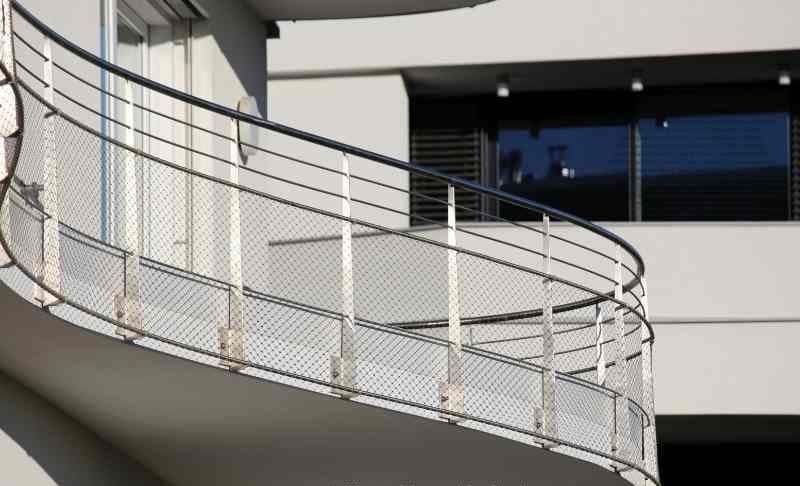 Geschwungenes Balkongeländer aus Edelstahl mit Drahtseilnetz-Füllung an einem weißen Neubau — Metallbau Tempelhof